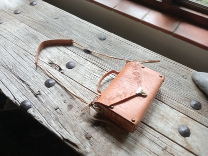 Brown leather pouch with metal clasps on a wooden surface